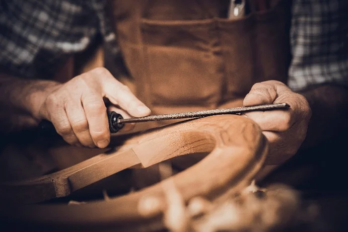 Hände feilen an einem Holzstück.